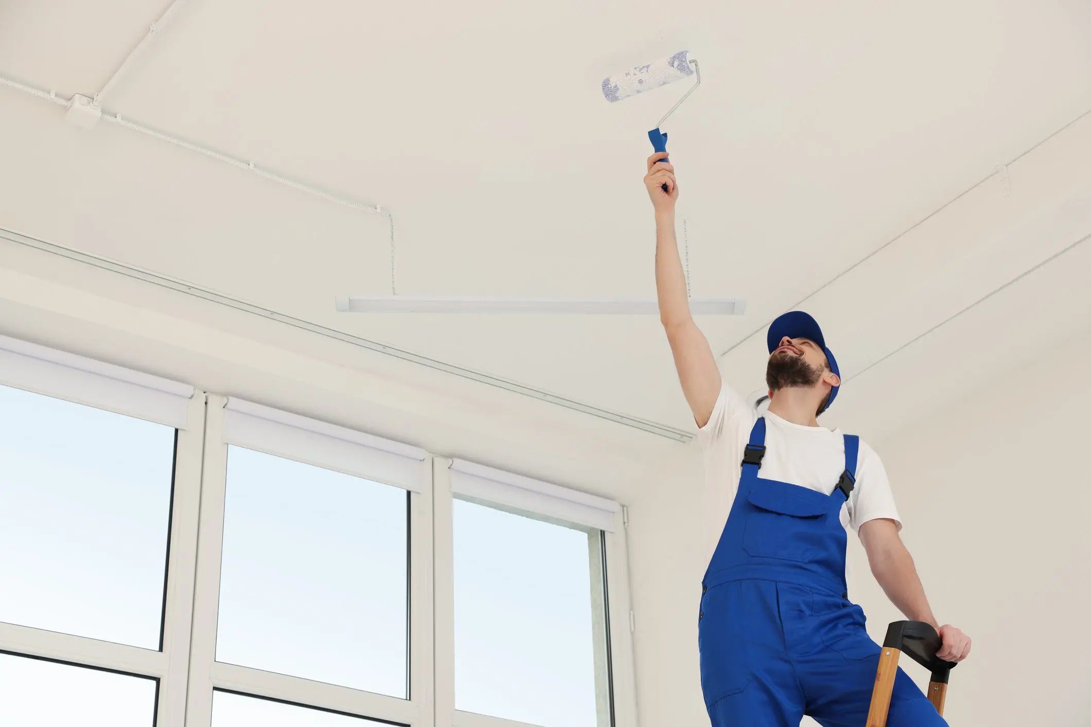 Man painting ceiling in blue overalls